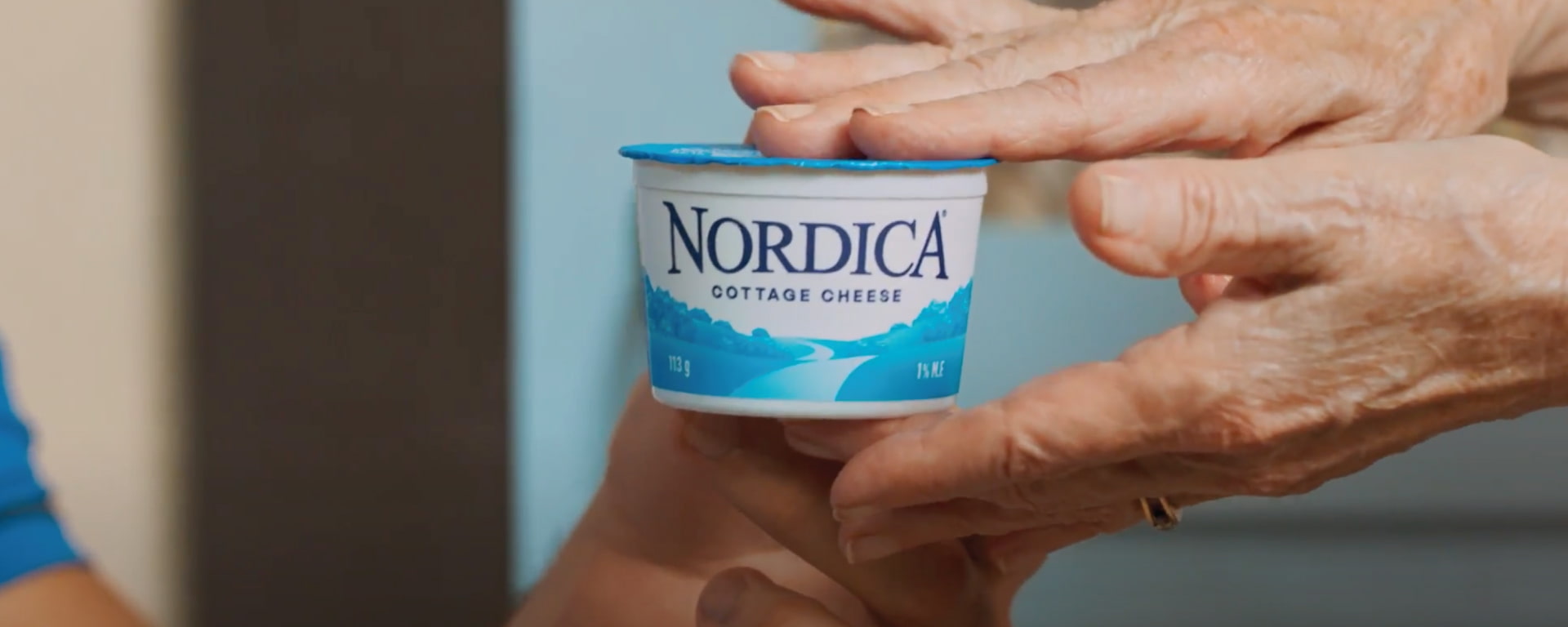 Two people passing Nordica On-the-Go Plain 1% cottage cheese